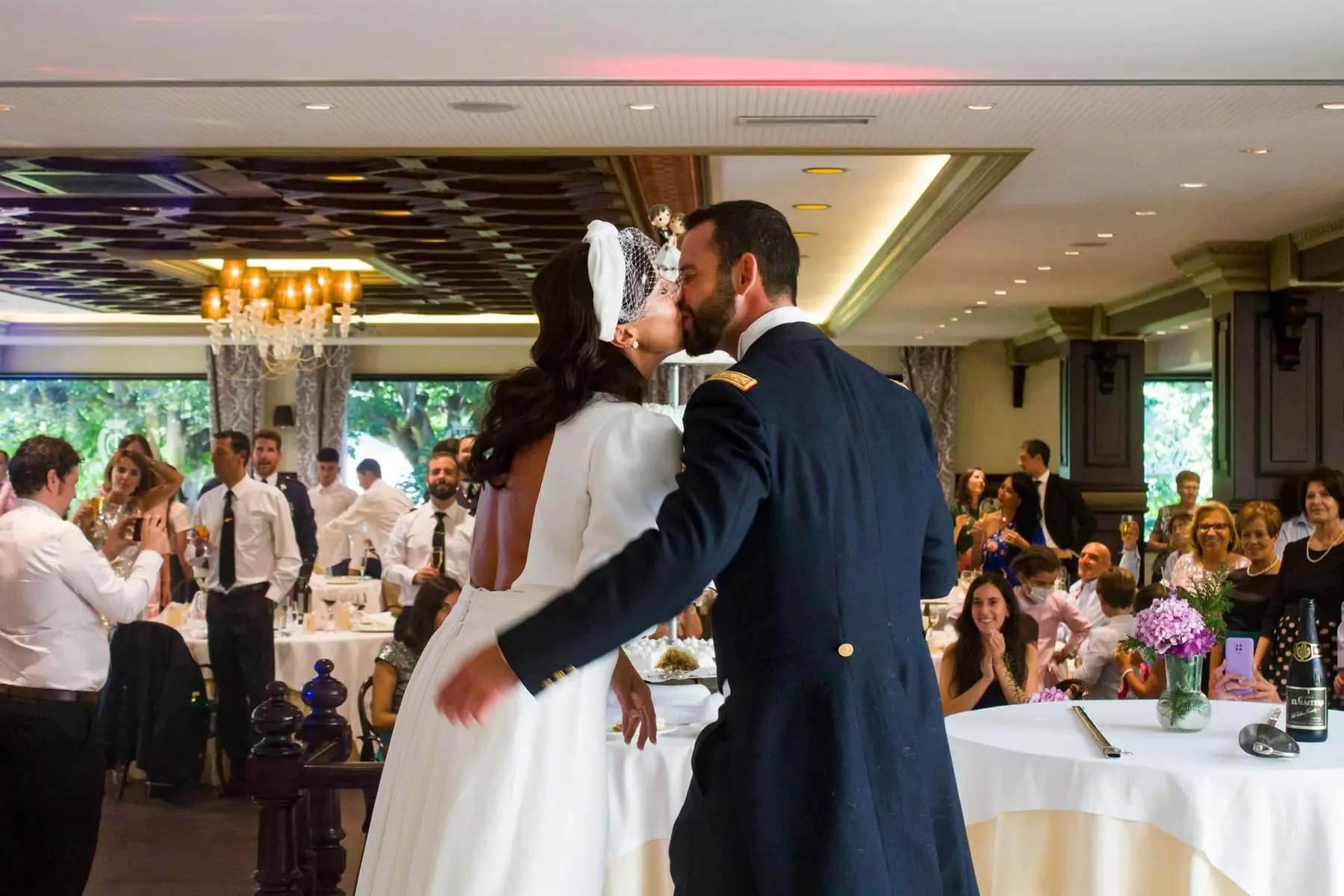 Un beso de los novios en medio de la sala, con los invitados alrededor