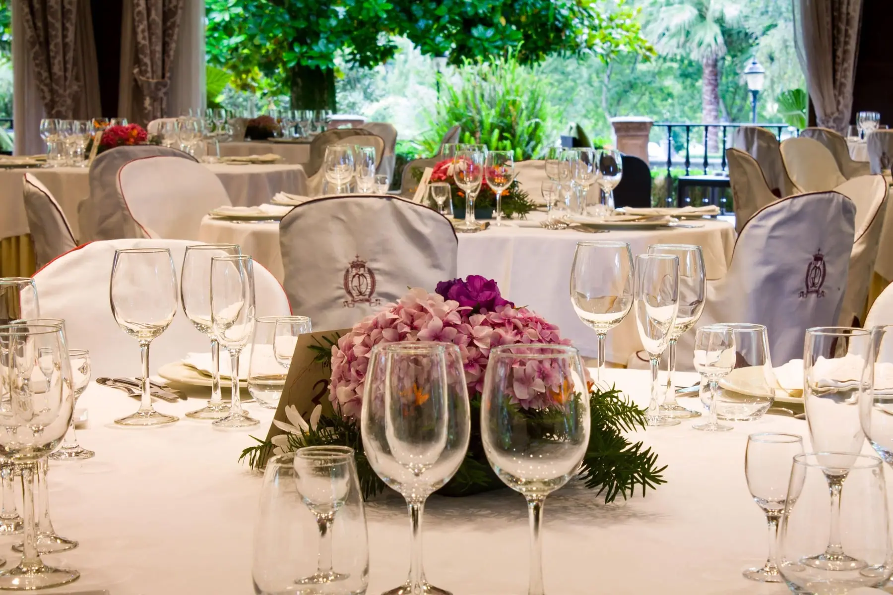 Una mesa con flores y copas, y el jardín al otro lado del cristal